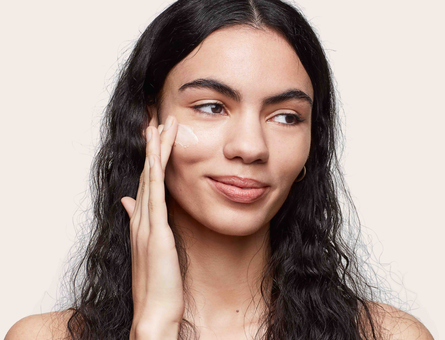 Woman using facial cream on her face looking to her side.