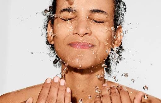 Female model splashing themselves with water to hydrate their skin