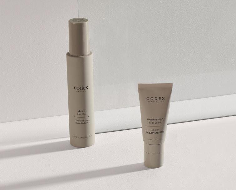 Image of bottles of Codex Beauty Labs Antü Radiance Mist and Antü Serum products on a beige background.