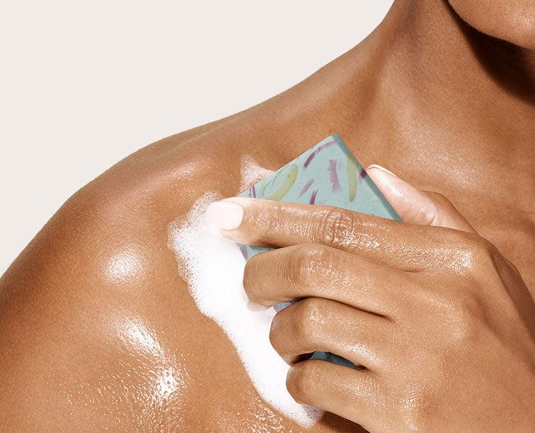 Image of a model using a bar of soap with suds on their shoulders