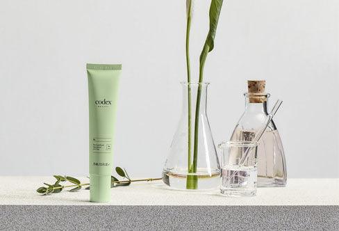 Codex Beauty Labs Bia Skin Superfood on a table surrounded by it ingredients and a scientific test tube and beaker. 