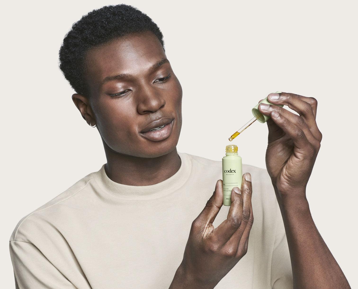 Male model holding a bottle of Bia Facial Oil and looking at the oil dropper