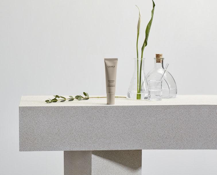 Codex Beauty Labs Antu Brightening Moisturizer sitting on a stone table surrounded by test tubes and a selection of natural ingredients