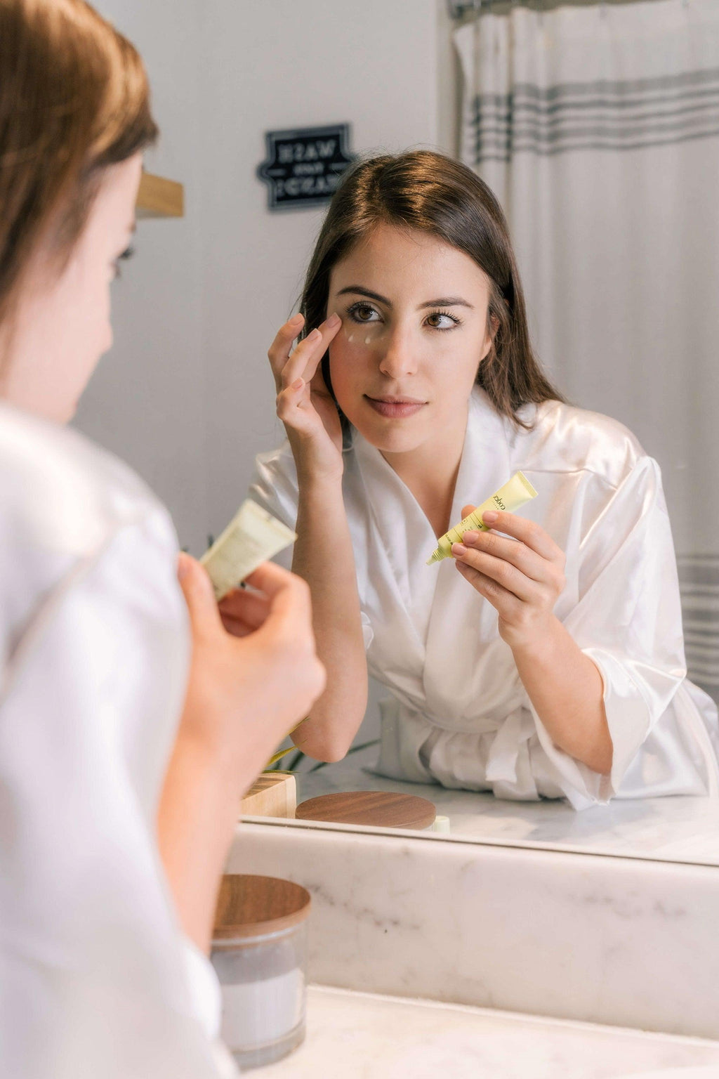Image of a female model applying Bia Eye Cream to her eyes in a mirror