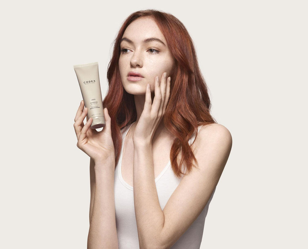 Female model holding the Antu Refreshing Gel Cleanser in one hand and touching her face with another hand