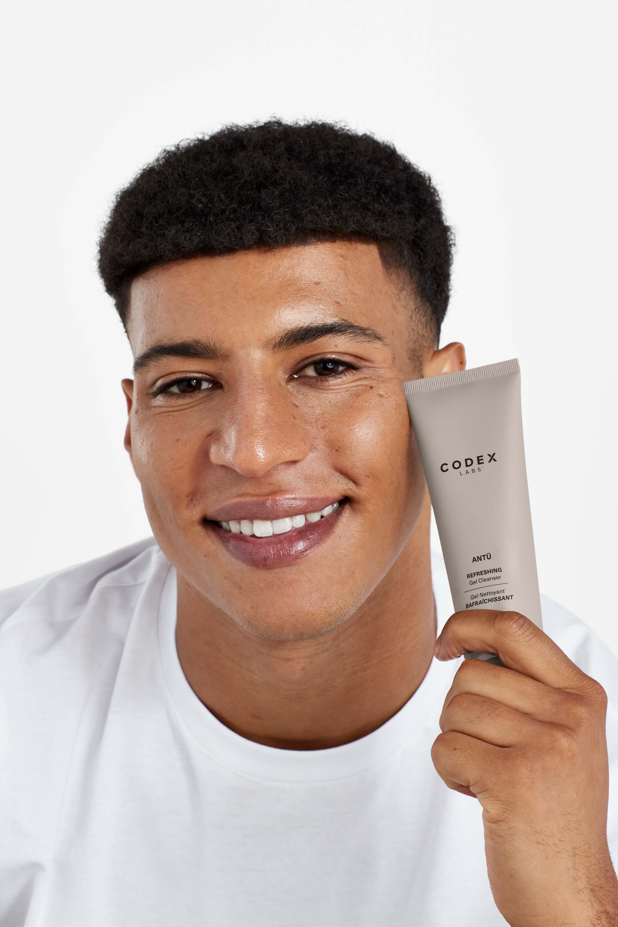 A smiling man in a white shirt hold Antü Refreshing Gel Cleanser.