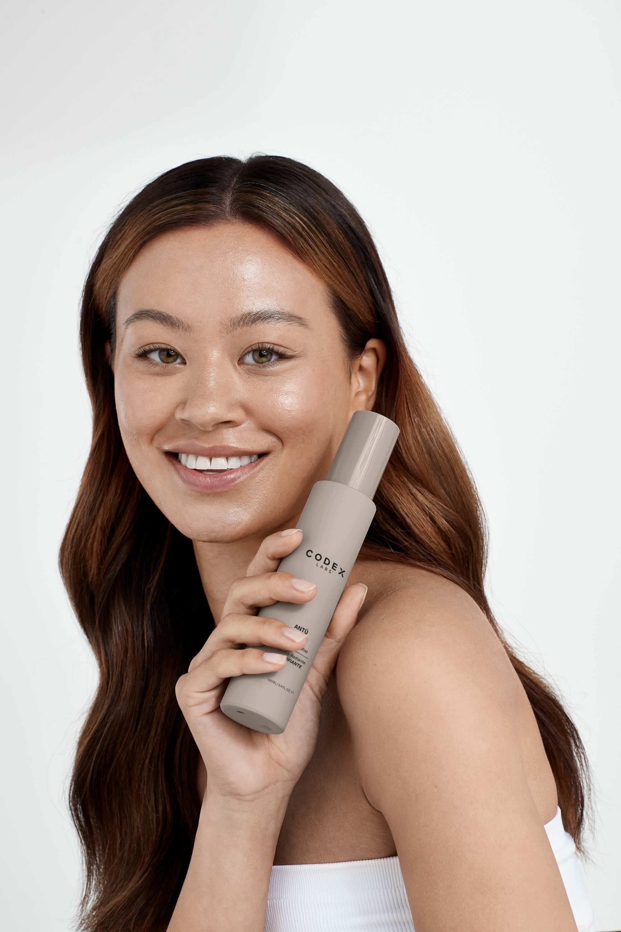 Woman smiling holding a bottle of Antü Radiance Mist.