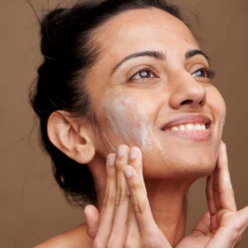 A woman rubbing a cream on her face while looking upwards.
