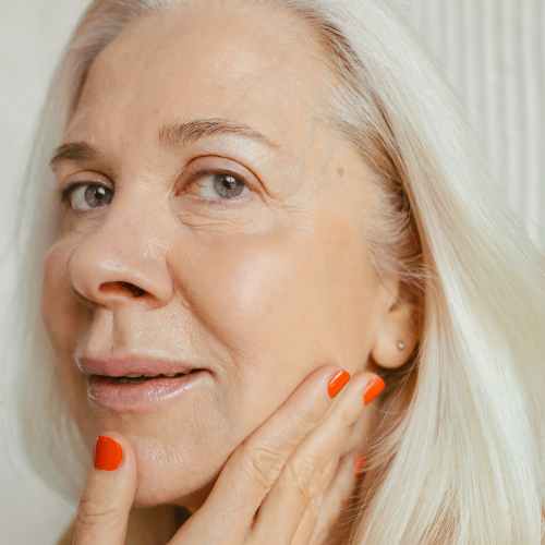 A blond woman with red fingernails touching her face.