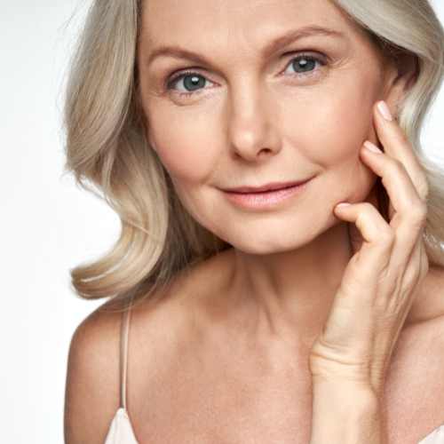 A blue eyed blond woman touching her face with her hand.