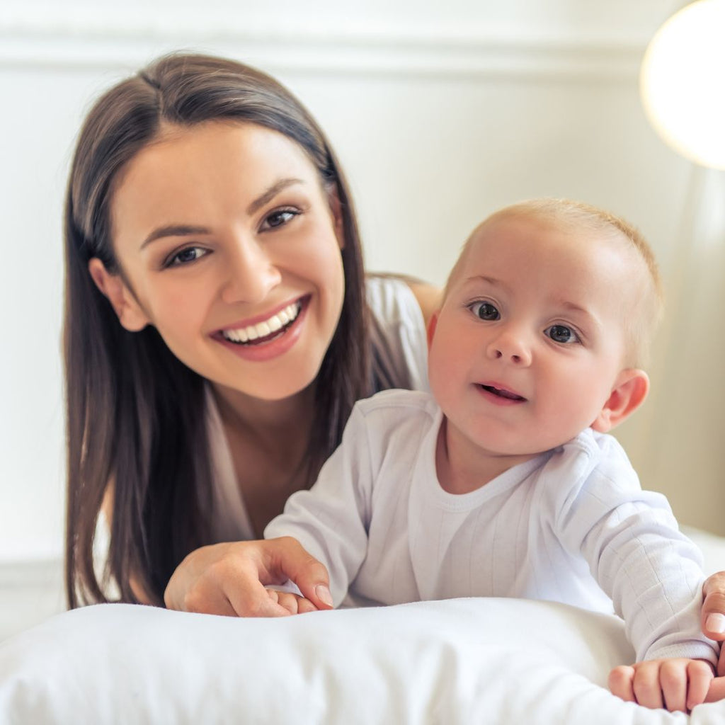 A mother with her baby on a bed smiling.
