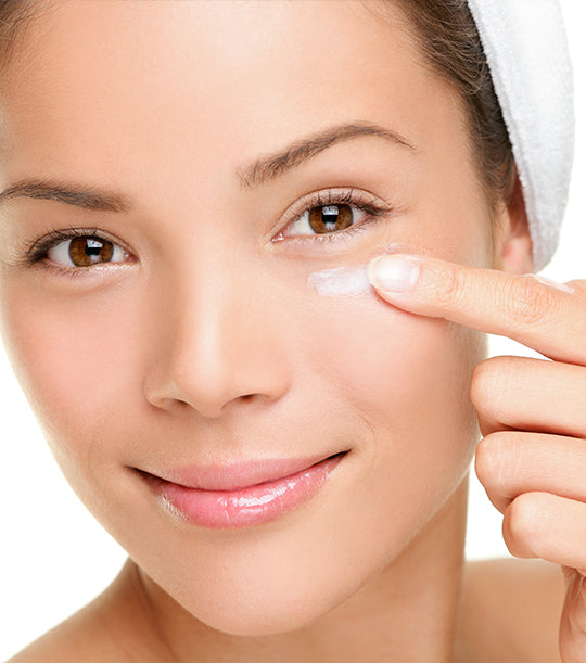 Image of a female model placing a cream eye cream under her eye. 